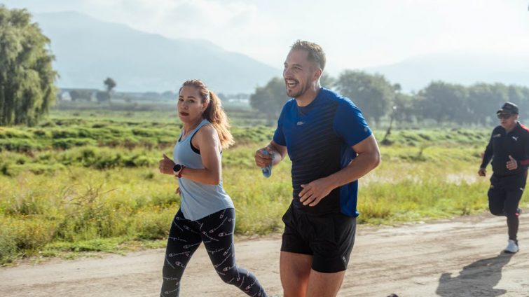 Two adults running on a rural dirt path, enjoying a sunny day outdoors.
